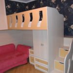 Sopra il divano rosso si trovano un mobile a muro e un letto a soppalco.