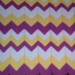 Una coperta bianca, gialla e lilla con un motivo a zigzag decorerà il tuo interno