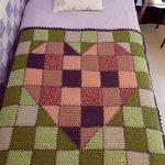 Cuvertură cu o inimă pe un fundal verde, realizată din elemente tricotate