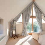 Tende grigie lunghe fino al pavimento per una finestra triangolare della soffitta